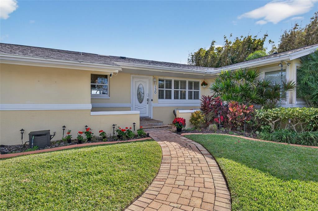 A brick walkway leads to the front entrance of a yellow house with white trim — 130 REEF ROAD, SOUTH DAYTONA, FL