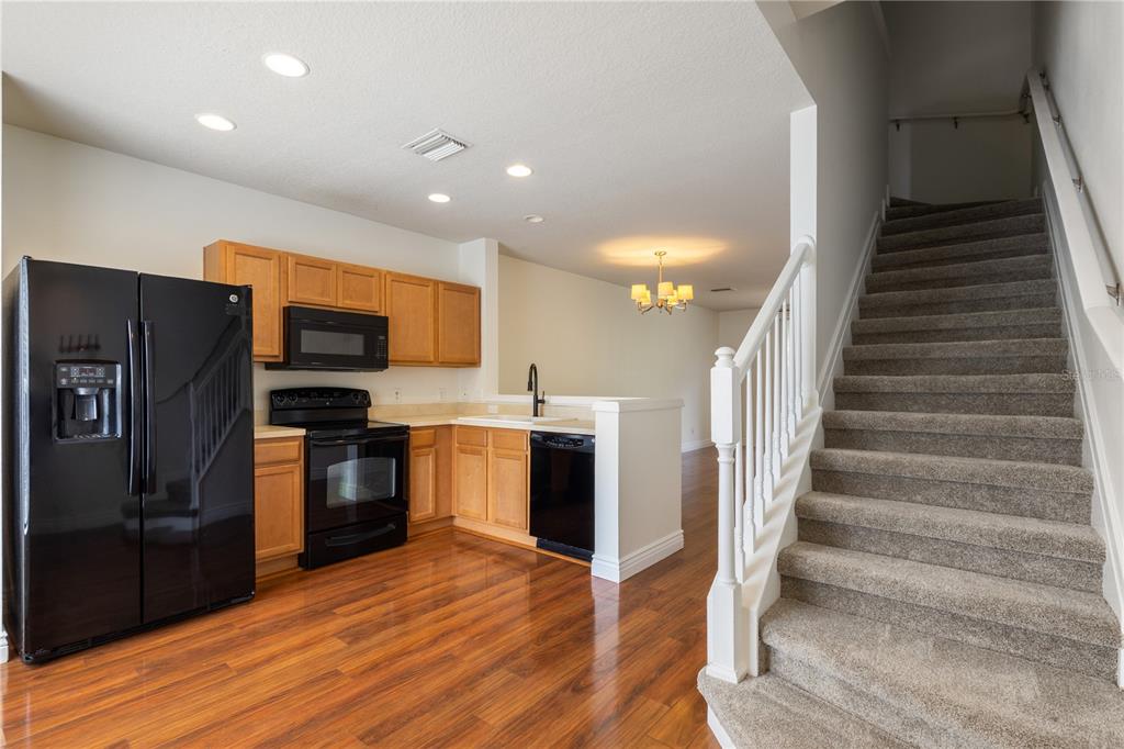 A kitchen with wood cabinets and black appliances sits next to a carpeted staircase — 10445 WESTPARK PRESERVE BOULEVARD, TAMPA, FL