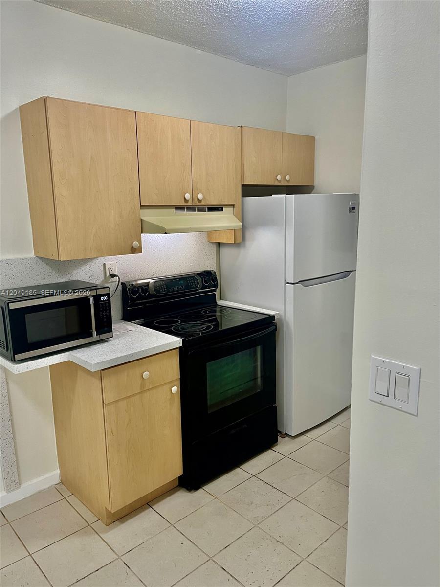 A small kitchen features light wood cabinets, a black electric stove, and a white refrigerator — 15699 SW 73rd Cir Ter # 11, Miami FL 33193, MIAMI, FL