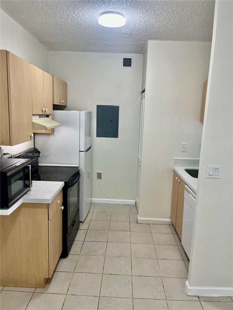A galley kitchen features light wood cabinets, white appliances, and beige tile flooring — 15699 SW 73rd Cir Ter # 11, Miami FL 33193, MIAMI, FL
