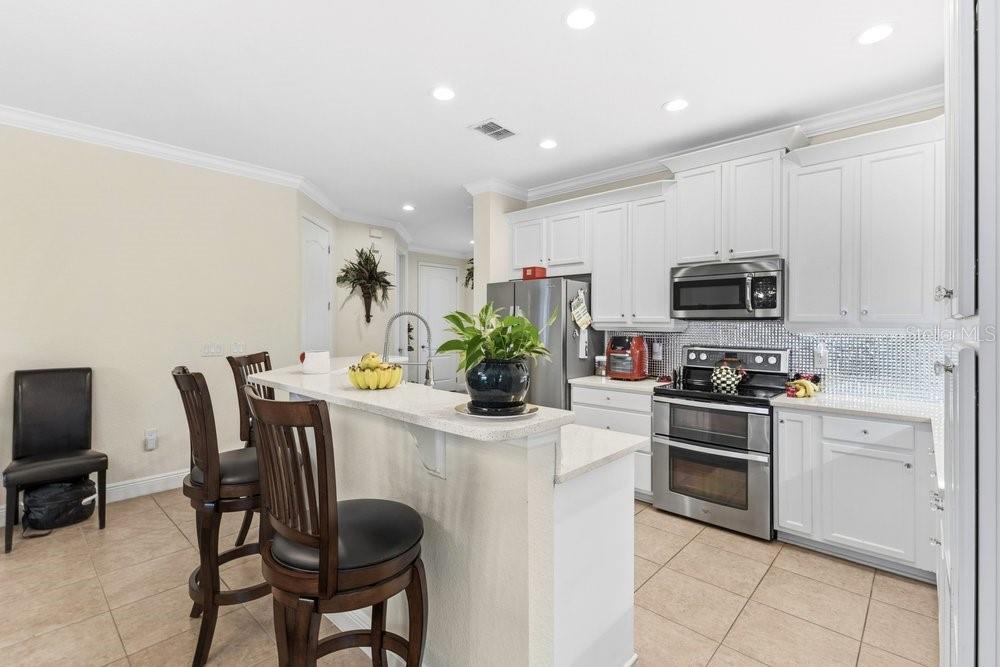 A kitchen with white cabinets, stainless steel appliances, and a breakfast bar with two chairs — 10722 BELFRY CIRCLE, ORLANDO, FL