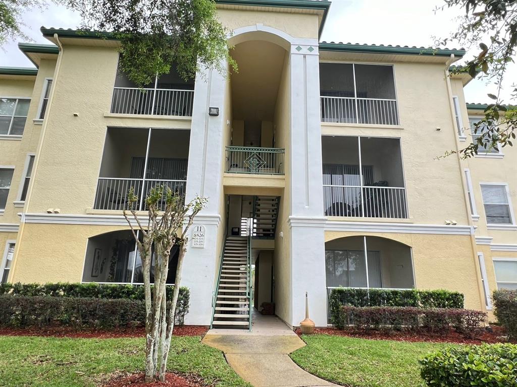 A three-story apartment building with screened balconies, a central staircase, and light yellow stucco siding — 8826 DUNES COURT UNIT 207, KISSIMMEE, FL