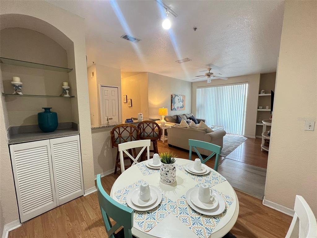 A dining area with a round table leads into a living room with a sliding door — 8826 DUNES COURT UNIT 207, KISSIMMEE, FL