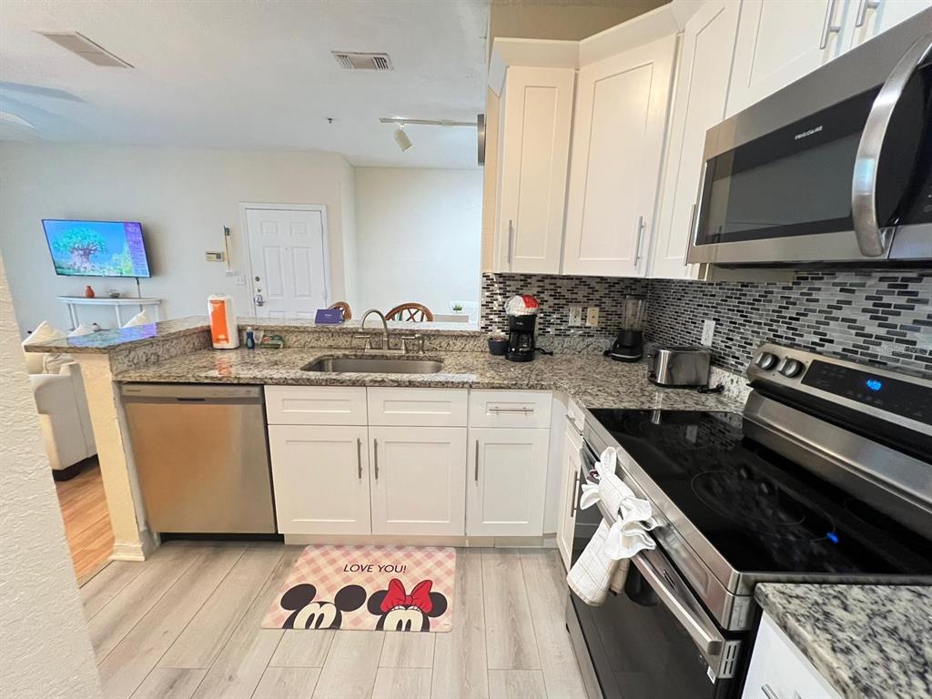 A kitchen features white cabinets, granite countertops, stainless steel appliances, and a Minnie Mouse mat — 8826 DUNES COURT UNIT 207, KISSIMMEE, FL