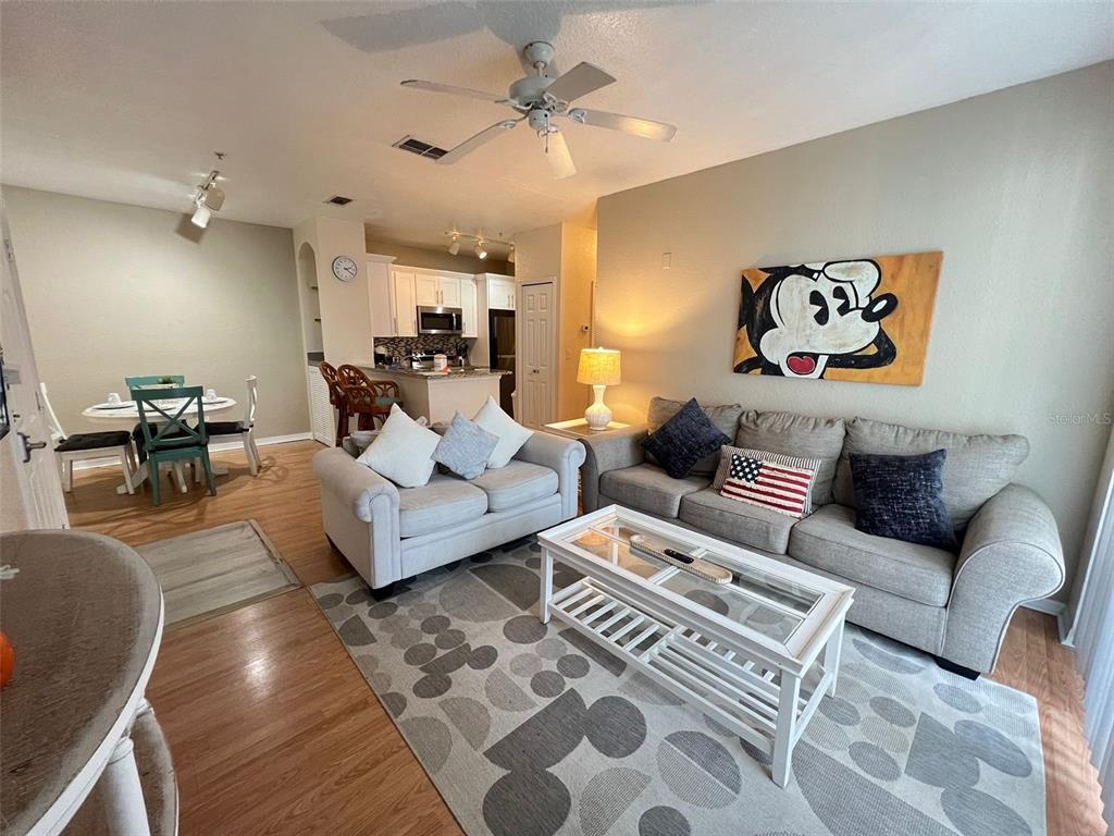 A living room and dining area feature light wood floors, gray furniture, and Mickey Mouse decor — 8826 DUNES COURT UNIT 207, KISSIMMEE, FL