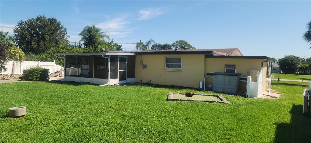 The exterior of a yellow house features a screened-in porch and a grassy backyard — 1700 MORNING DOVE LANE, ENGLEWOOD, FL