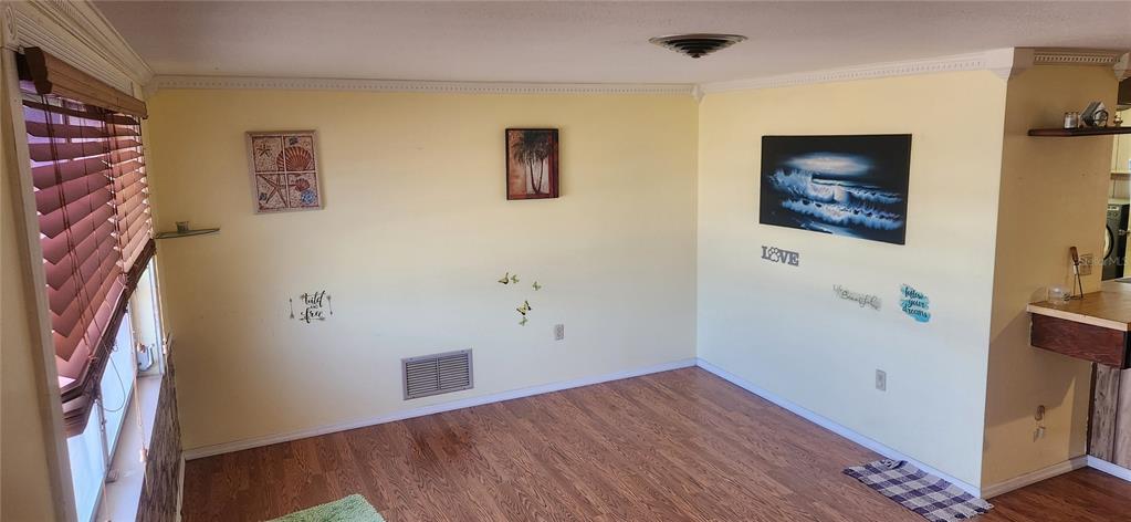 A room with light yellow walls, wood-look flooring, window blinds, and several wall decorations — 1700 MORNING DOVE LANE, ENGLEWOOD, FL