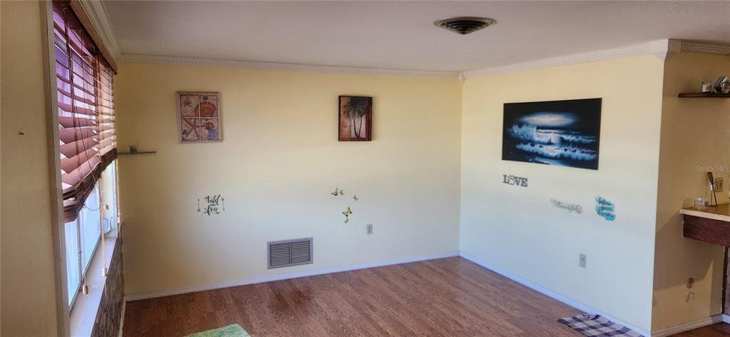 A room with yellow walls, wood-look flooring, a window with blinds, and several wall decorations — 1700 MORNING DOVE LANE, ENGLEWOOD, FL