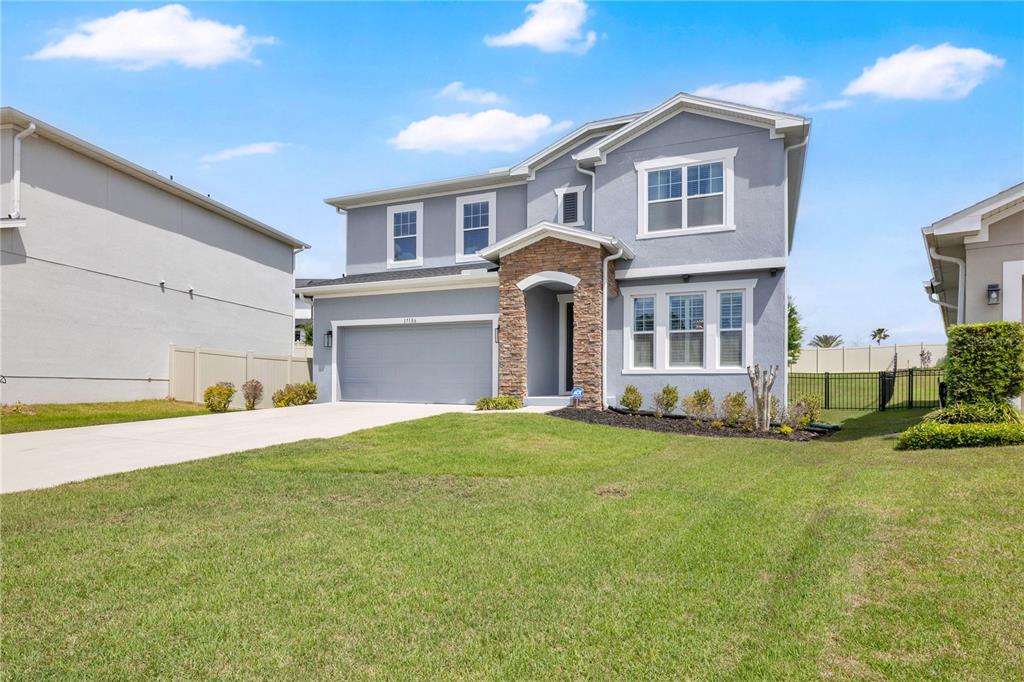 A two-story gray house features a stone-accented entryway, a two-car garage, and a lawn — 17186 HICKORY WIND DRIVE, CLERMONT, FL