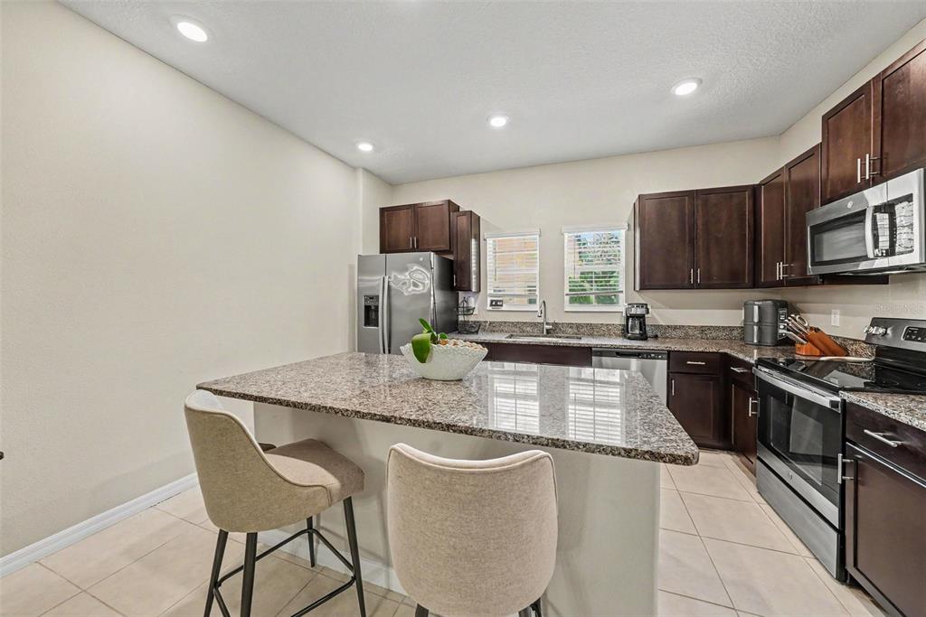 A kitchen features dark wood cabinets, granite countertops, stainless steel appliances, and a breakfast bar — 4524 TUSCAN LOON DRIVE, TAMPA, FL