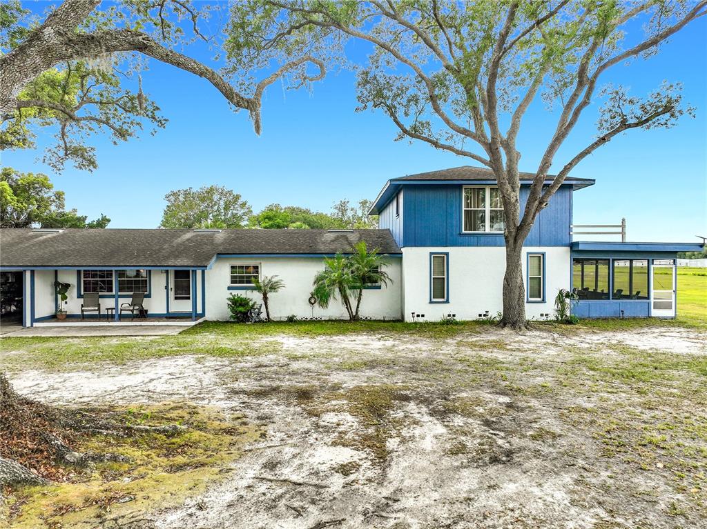 A two-story house with white and blue siding stands on a sandy, tree-filled lot — 7001 JONES AVENUE, MOUNT DORA, FL