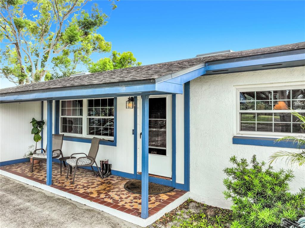 A covered porch with tiled flooring and two chairs sits in front of a house — 7001 JONES AVENUE, MOUNT DORA, FL