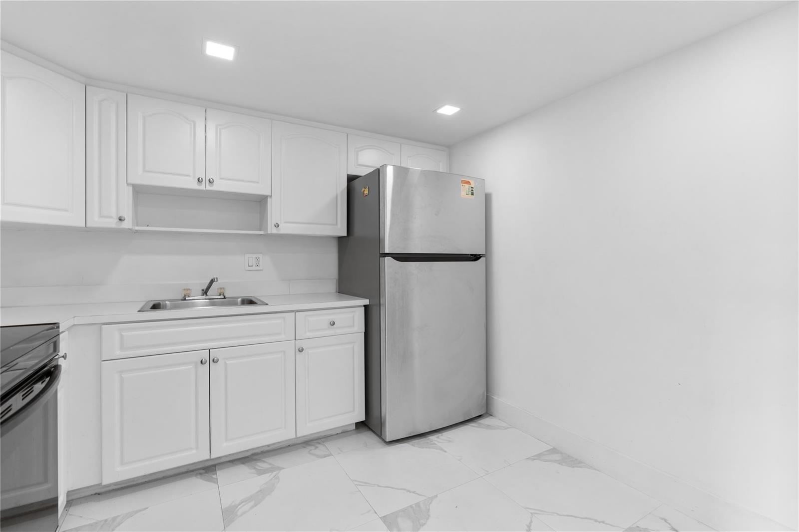A small kitchen features white cabinets, a stainless steel refrigerator, and white tiled flooring — 4164 Inverrary Drive # 412, Lauderhill FL 33319, LAUDERHILL, FL