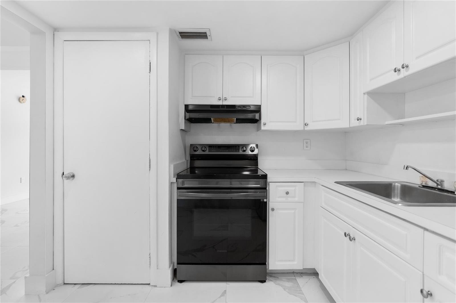 A kitchen features white cabinets, a black stove, and a stainless steel sink — 4164 Inverrary Drive # 412, Lauderhill FL 33319, LAUDERHILL, FL