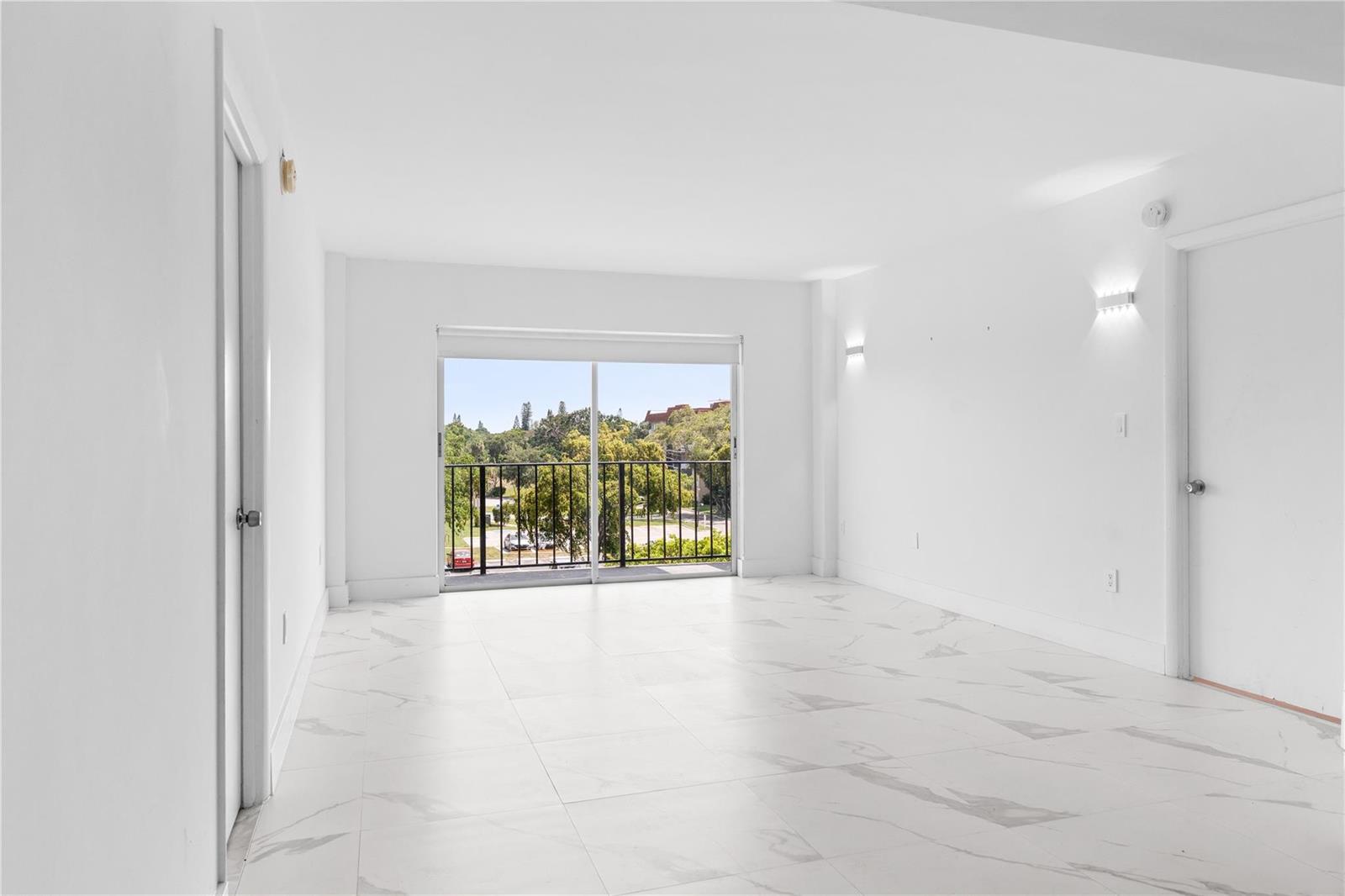 An empty room with white walls, white marble-look tile flooring, and a sliding glass balcony door — 4164 Inverrary Drive # 412, Lauderhill FL 33319, LAUDERHILL, FL