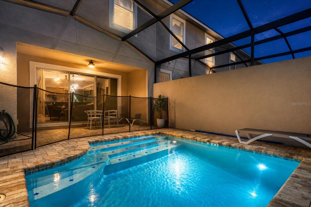 A small backyard swimming pool with steps is enclosed by a screen and safety fence — 1562 CAREY PALM CIRCLE, KISSIMMEE, FL