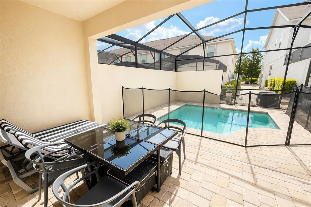 A covered patio features a dining set, lounge chairs, and a screened-in pool area — 1562 CAREY PALM CIRCLE, KISSIMMEE, FL