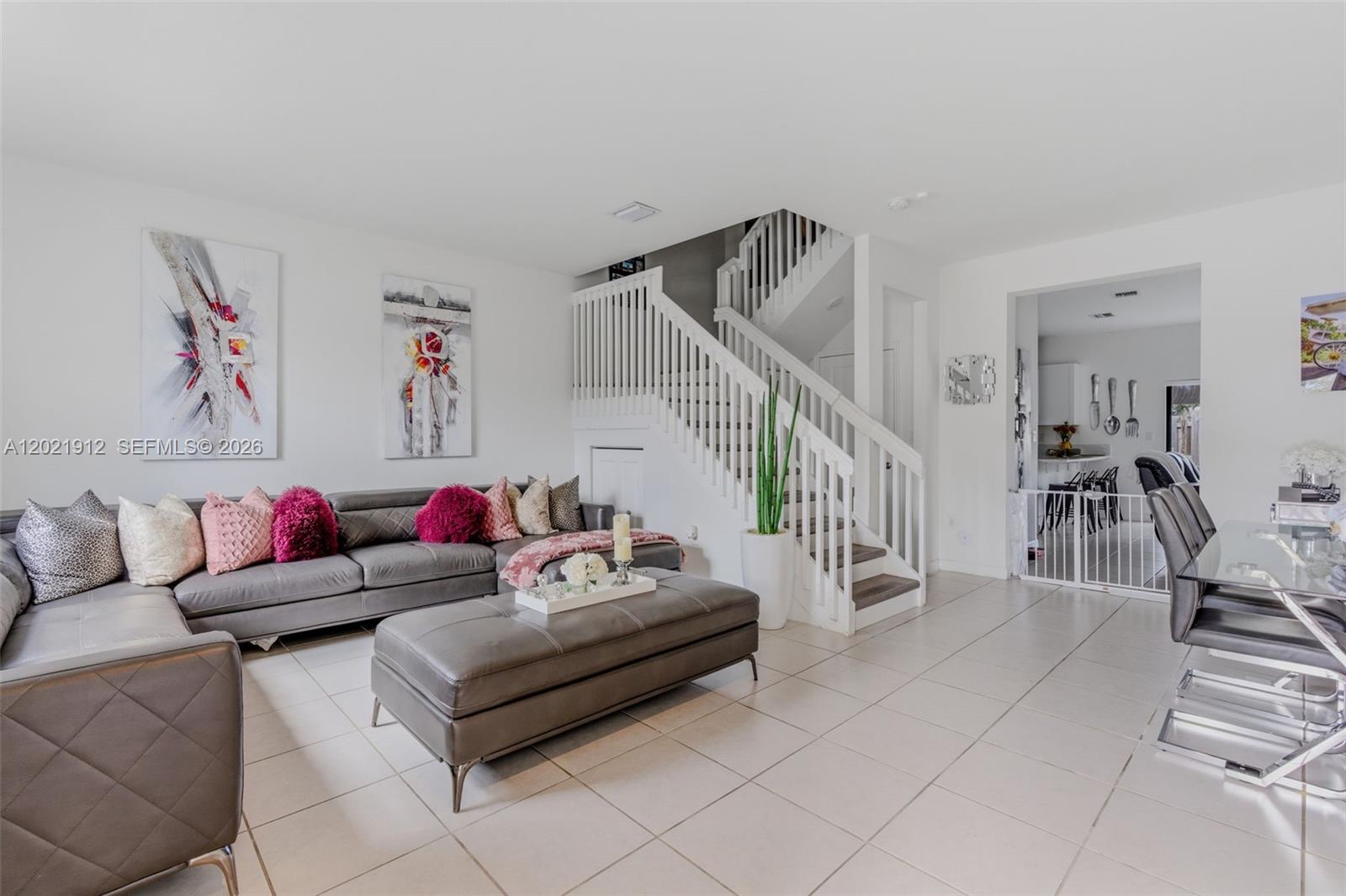 A living room with a grey sectional sofa, large ottoman, and a staircase with white railings — 10009 SW 228th Ter, Miami FL 33190, MIAMI, FL