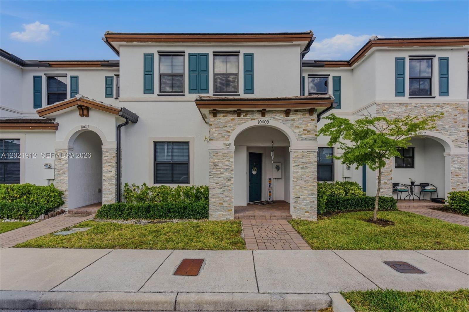 A row of two-story townhouses features white stucco walls, stone-accented entryways, and teal window shutters — 10009 SW 228th Ter, Miami FL 33190, MIAMI, FL