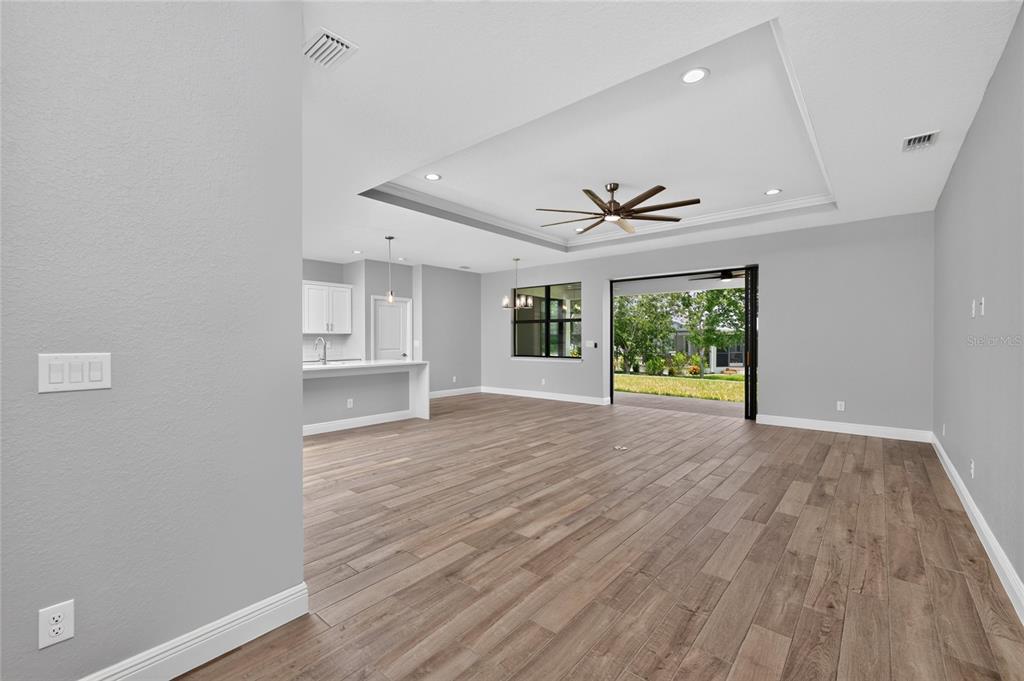 An open-concept living area features wood-look tile floors, a tray ceiling, and sliding glass doors — 9590 HONEYMOON DRIVE, PORT CHARLOTTE, FL