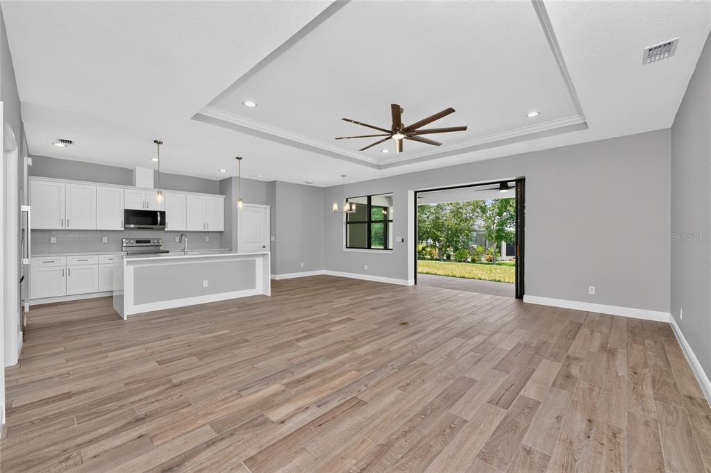 An open-concept kitchen and living area with gray walls, white cabinetry, and wood-look tile flooring — 9590 HONEYMOON DRIVE, PORT CHARLOTTE, FL