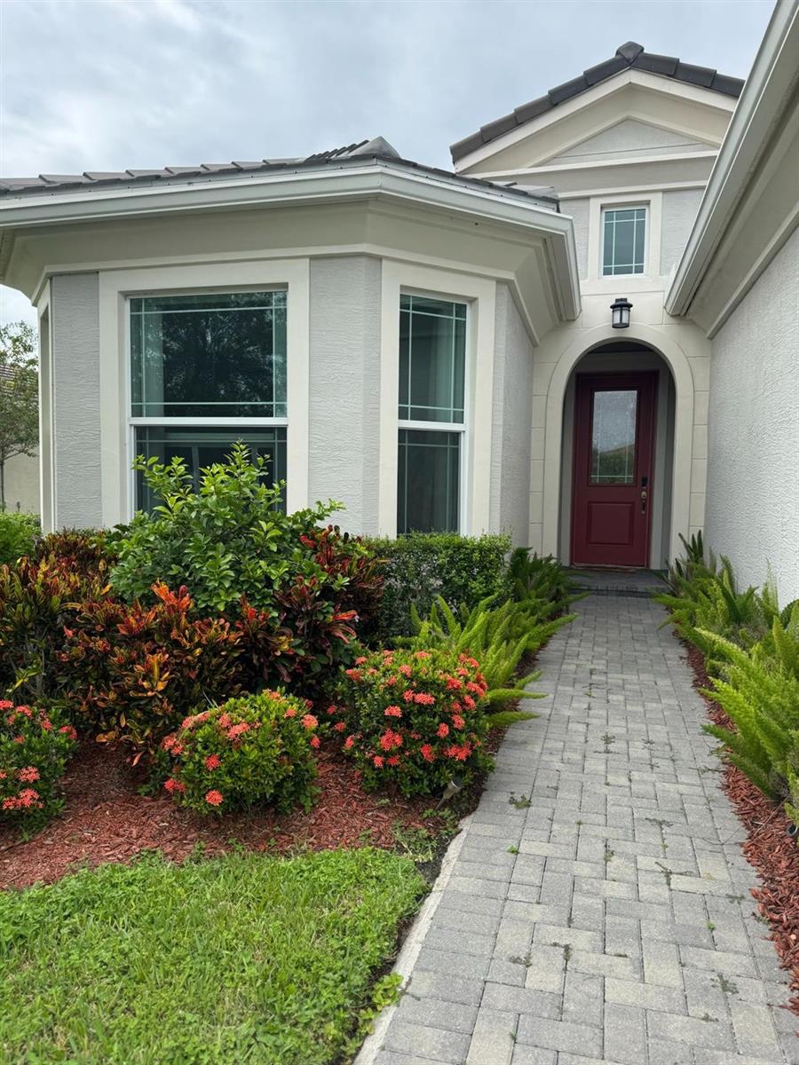 A red front door is set within an arched entryway next to a landscaped garden — 16117 Whippoorwill Circle, Westlake FL 33470, WESTLAKE, FL