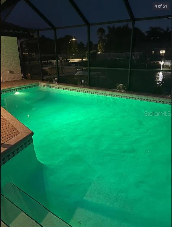 An illuminated swimming pool at night is enclosed by a screened lanai overlooking a canal — 2001 HAWAII AVENUE NE, ST PETERSBURG, FL