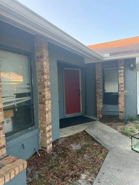 A red front door is set between two brick columns on a gray exterior wall — 4604 FERN PINE DRIVE, ORLANDO, FL