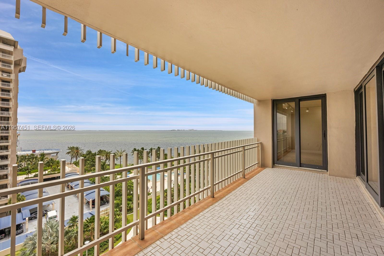 A balcony with a tiled floor and metal railing overlooks the ocean and palm trees — 2 Grove Isle Dr # B907, Miami FL 33133, MIAMI, FL
