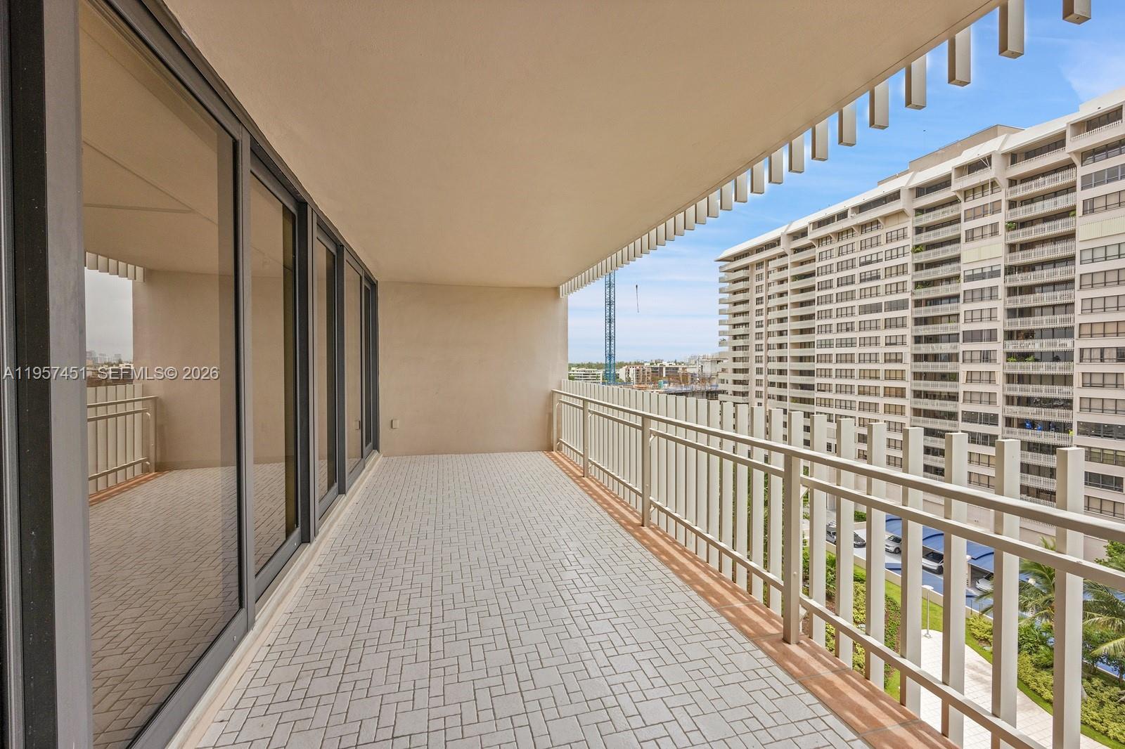 A covered balcony features light-colored tiled flooring, a metal railing, and views of nearby buildings — 2 Grove Isle Dr # B907, Miami FL 33133, MIAMI, FL