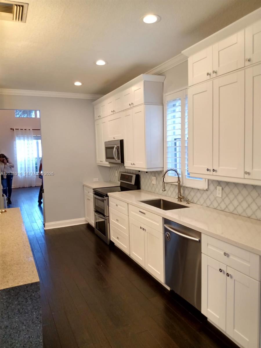 A kitchen features white cabinets, stainless steel appliances, a tile backsplash, and dark wood flooring — 8682 Via Ancho Rd, Boca Raton FL 33433, BOCA RATON, FL