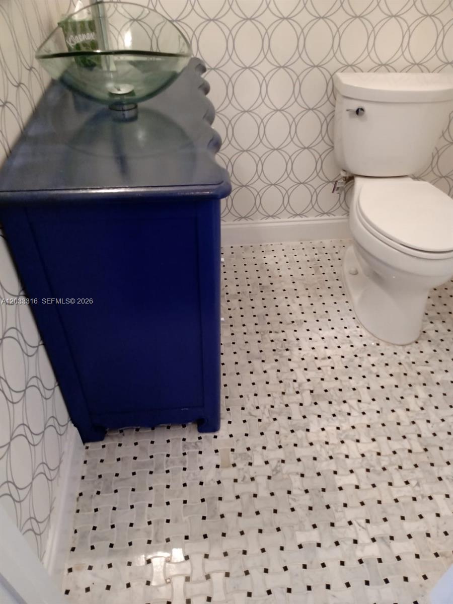 A bathroom features a blue vanity with a glass sink, patterned wallpaper, and tiled flooring — 8682 Via Ancho Rd, Boca Raton FL 33433, BOCA RATON, FL
