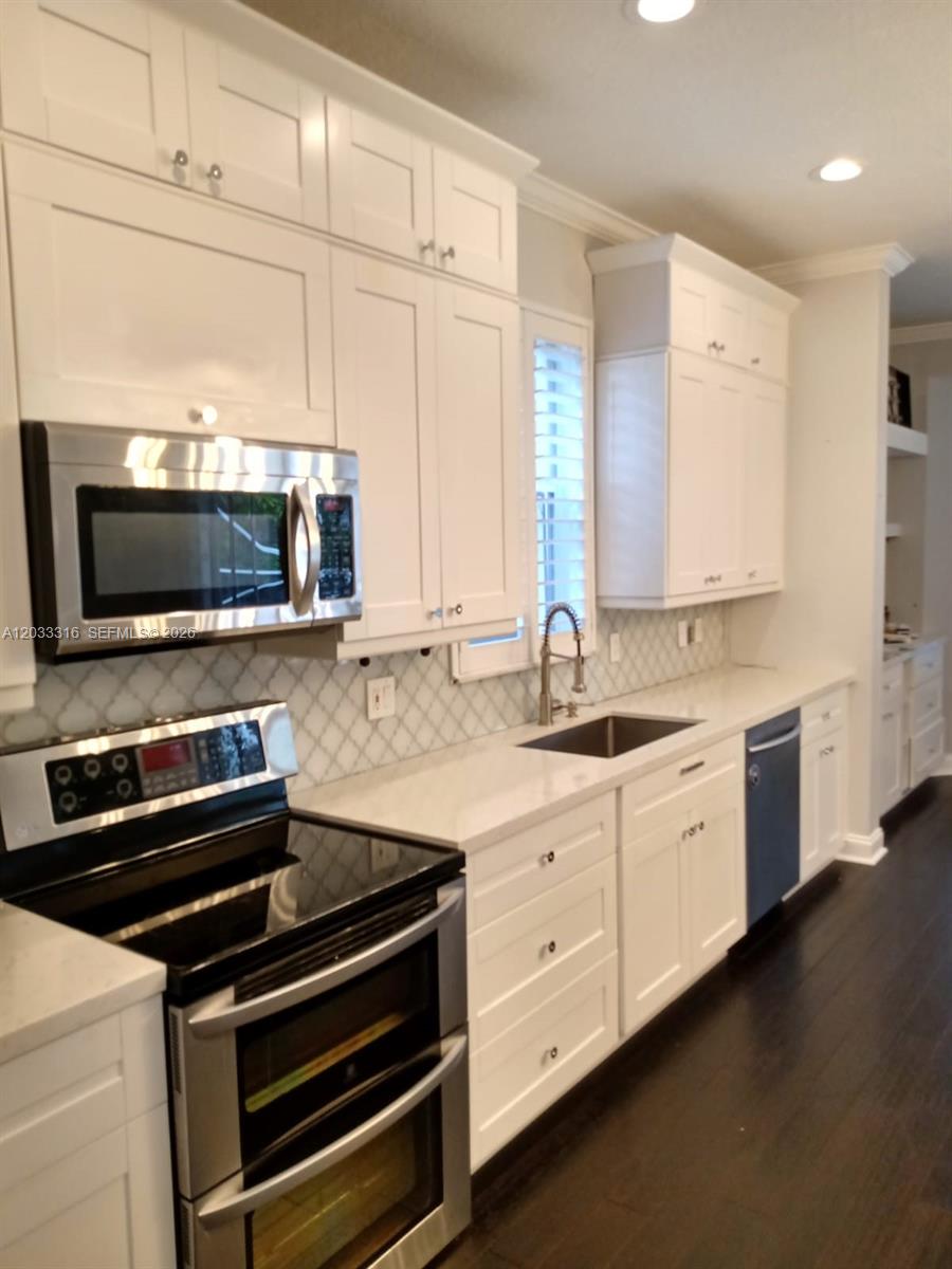 A kitchen features white shaker cabinets, stainless steel appliances, a tile backsplash, and dark flooring — 8682 Via Ancho Rd, Boca Raton FL 33433, BOCA RATON, FL