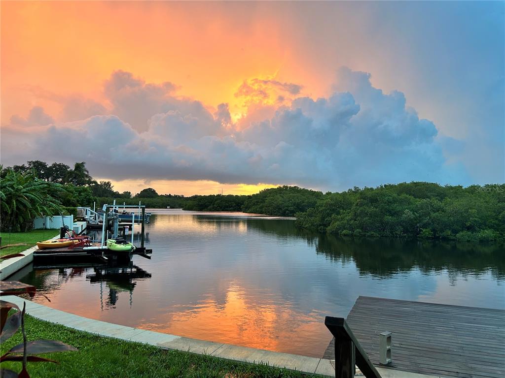 A waterfront view of a canal at sunset with a wooden dock and boat lift — 2126 EGRET DRIVE, CLEARWATER, FL
