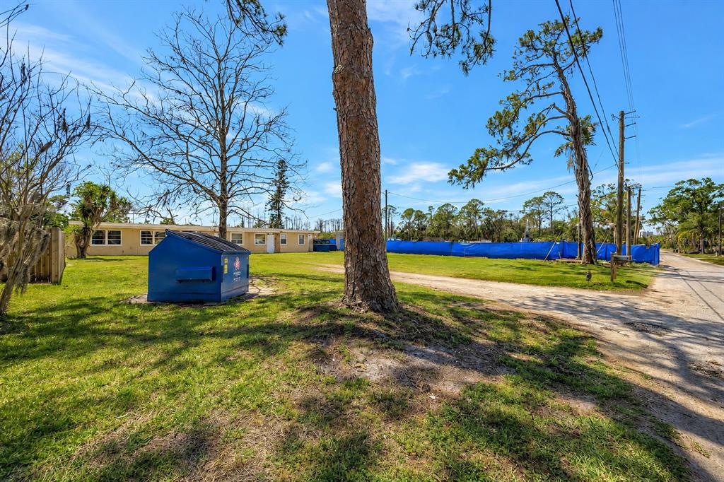 A blue dumpster sits on a grassy lot next to a building and blue fencing — 5100 SOUTH ROAD, NEW PORT RICHEY, FL