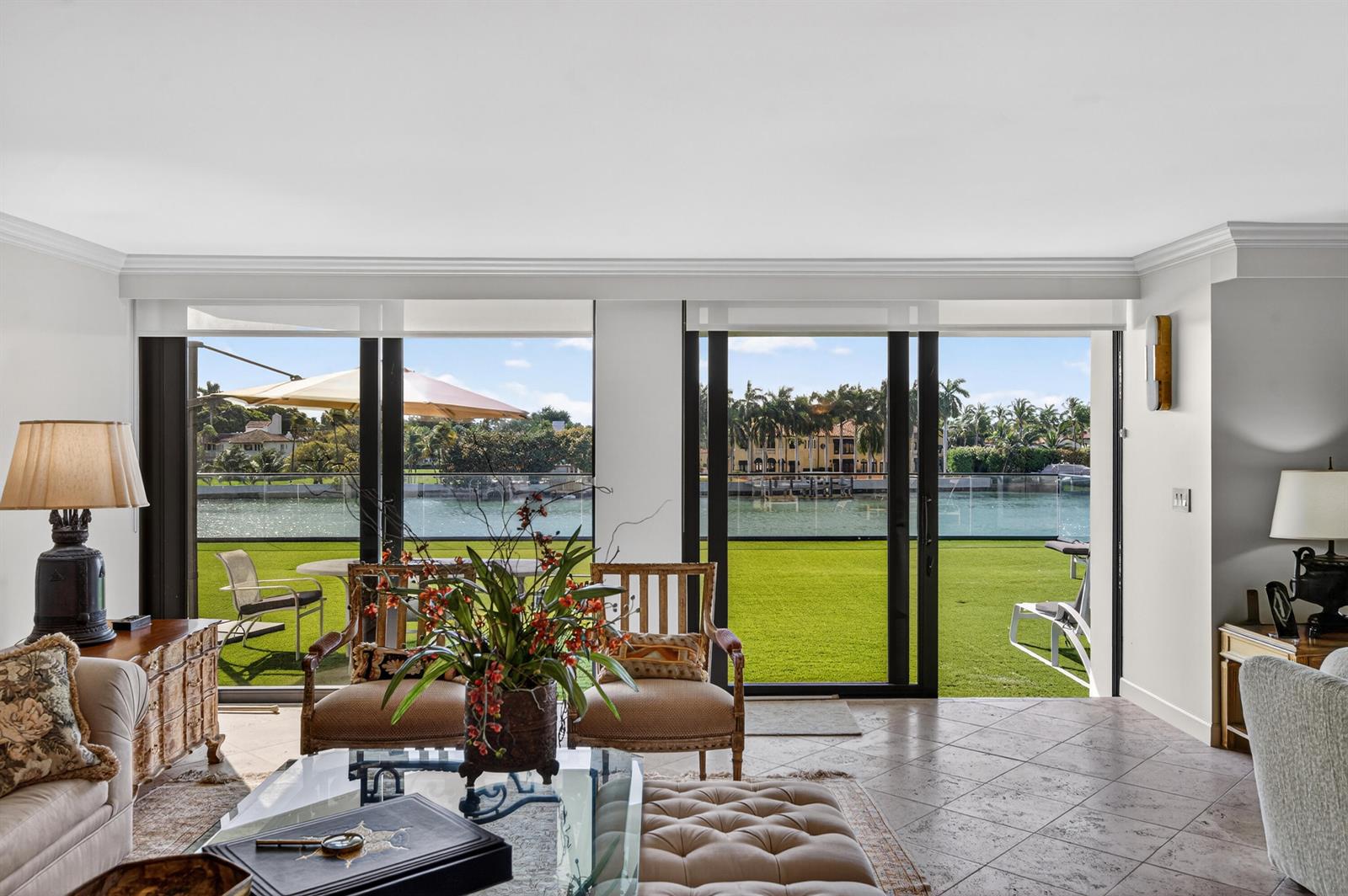 A living room with tile floors and sliding glass doors overlooking a lawn and canal — 5500 Collins Avenue # 302, Miami Beach FL 33140, MIAMI BEACH, FL