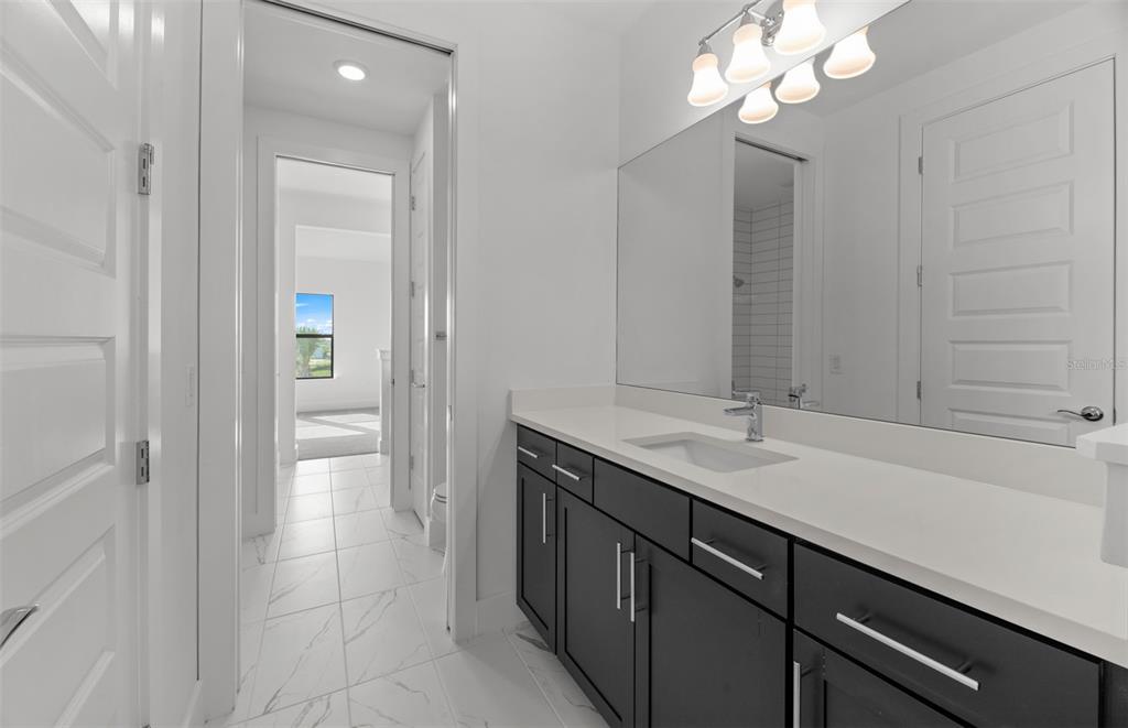 A bathroom features a dark vanity with a white countertop, large mirror, and tiled flooring — 16407 LILLY ELANIE WAY, BRADENTON, FL