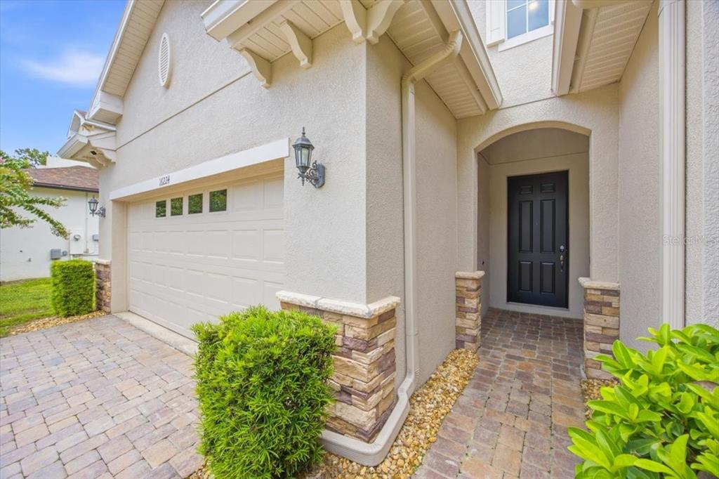 A beige house exterior features a two-car garage, a stone-accented entryway, and a dark door — 16224 SW MEAD STREET, CLERMONT, FL