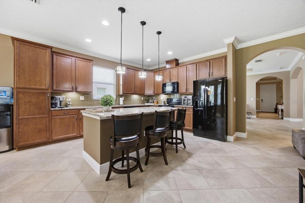A kitchen features wood cabinets, granite countertops, a central island with stools, and black appliances — 16224 SW MEAD STREET, CLERMONT, FL