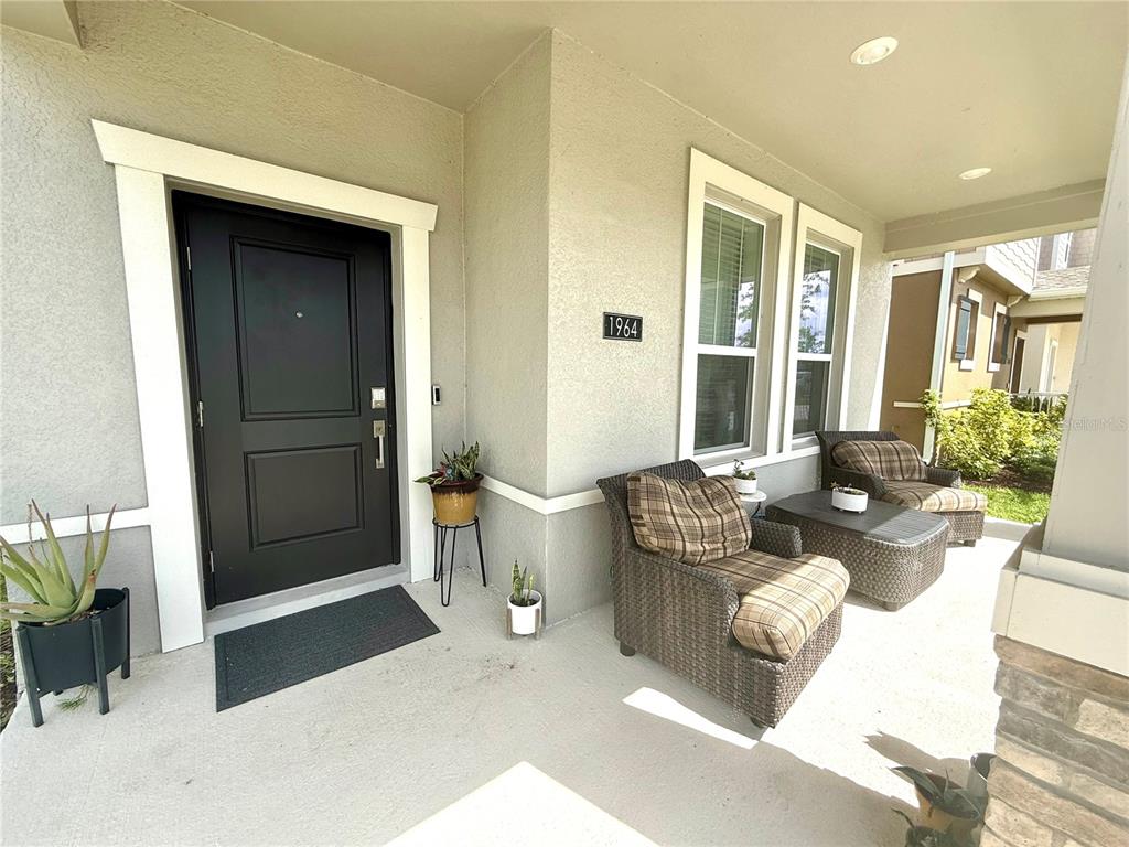 A covered front porch features a black door, two wicker chairs, and potted plants — 1964 TOHOQUA BOULEVARD, KISSIMMEE, FL