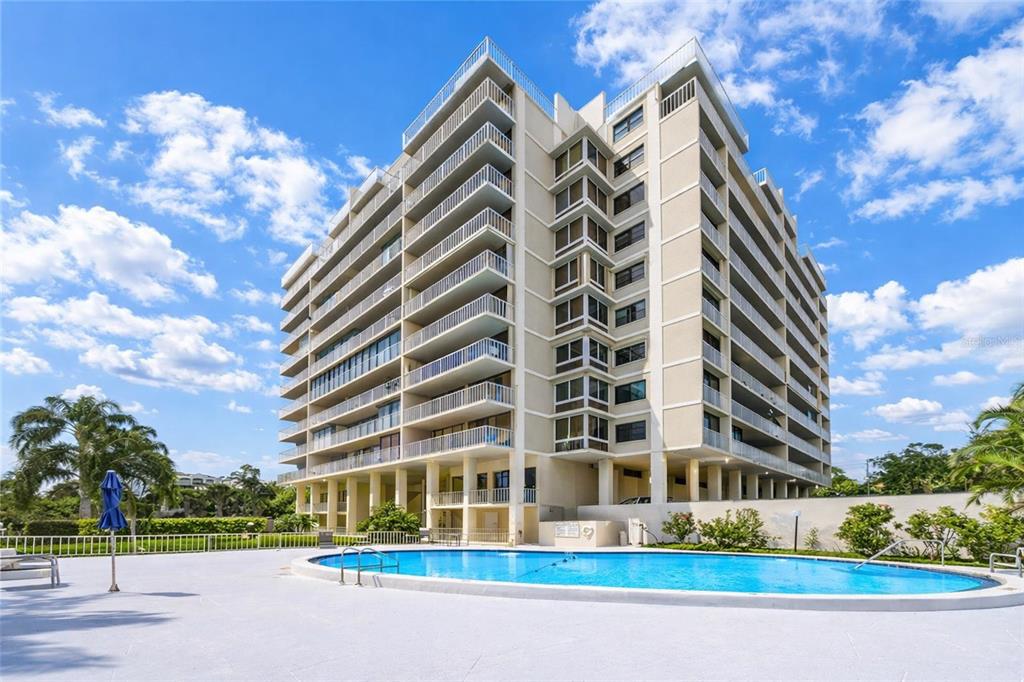 A multi-story apartment building stands behind a swimming pool under a blue sky — 500 N OSCEOLA AVENUE UNIT 307, CLEARWATER, FL