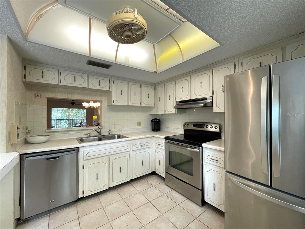 A kitchen features white cabinetry, stainless steel appliances, a tiled backsplash, and a ceiling fan — 840 VIRGINIA STREET UNIT 303, DUNEDIN, FL
