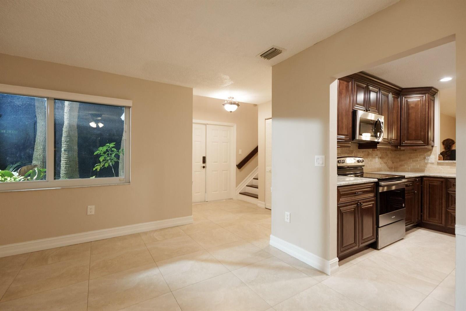 A kitchen with dark wood cabinets and stainless steel appliances opens to a tiled dining area — 7251 NW 24th Court, Margate FL 33063, MARGATE, FL