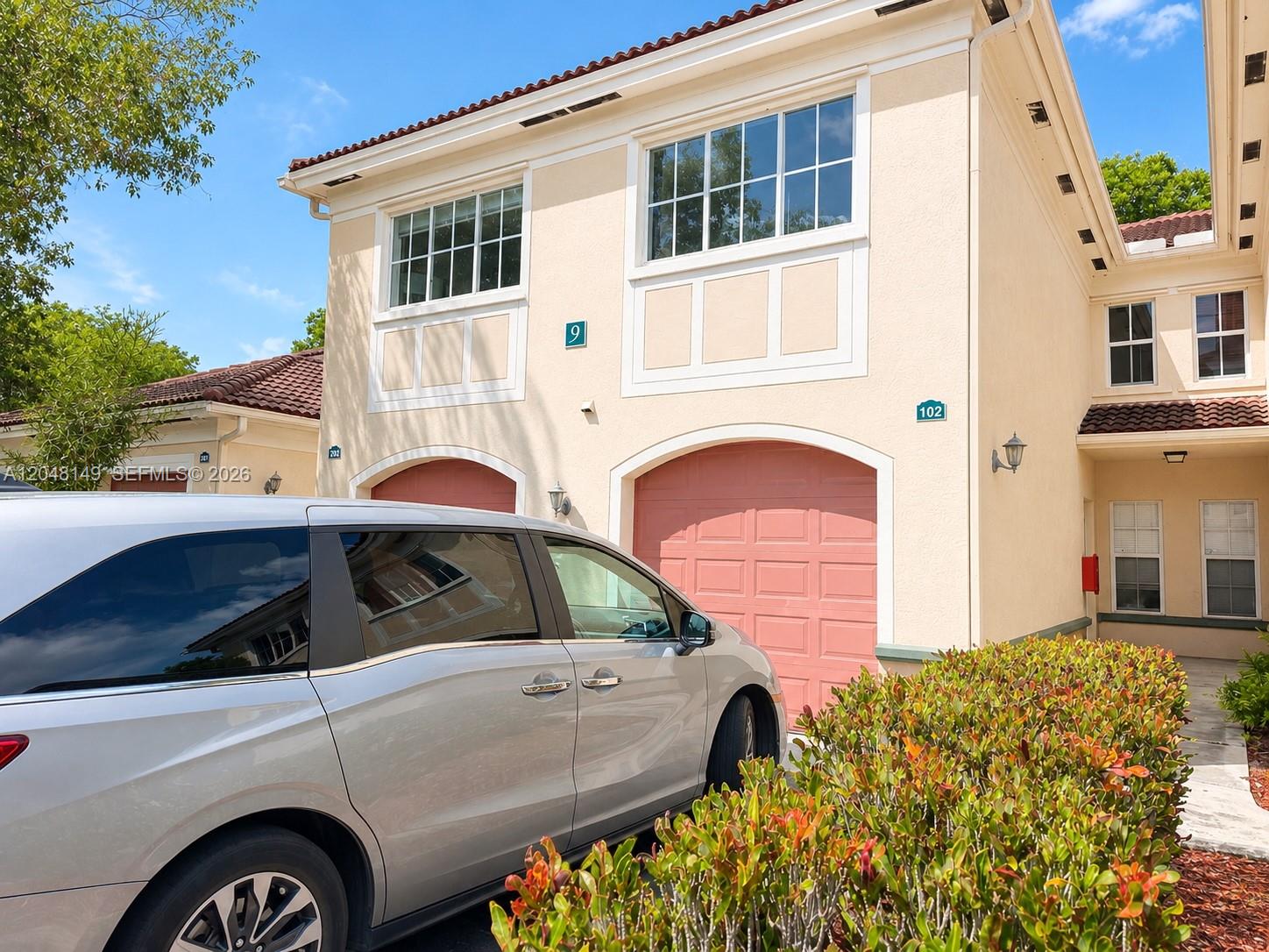A silver minivan is parked in front of a two-story beige townhouse with pink garage doors — 2452 Centergate Dr # 102, Miramar FL 33025, MIRAMAR, FL