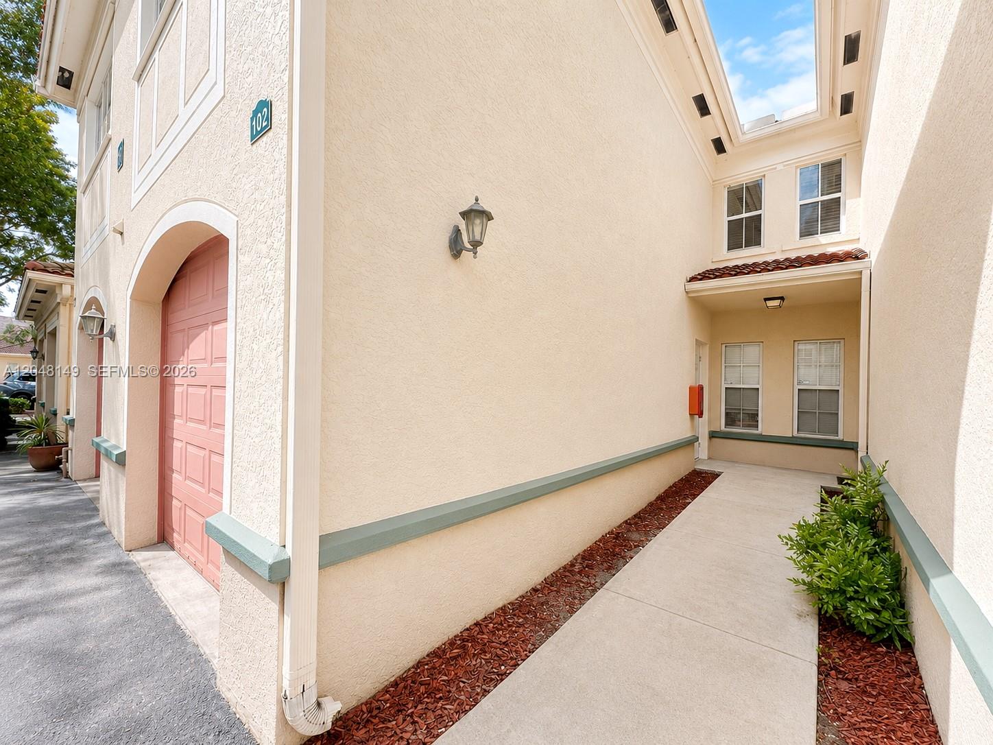 The exterior of a beige stucco building features a pink garage door and a walkway — 2452 Centergate Dr # 102, Miramar FL 33025, MIRAMAR, FL