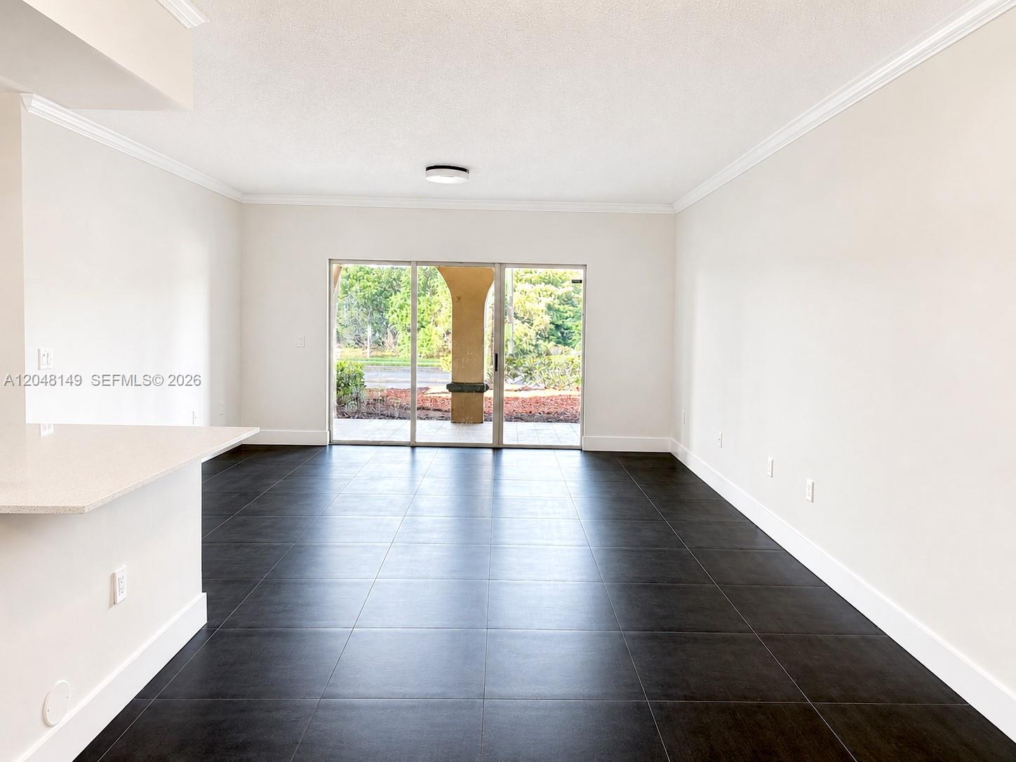 An empty living room features dark tile flooring, white walls, and a sliding glass door — 2452 Centergate Dr # 102, Miramar FL 33025, MIRAMAR, FL