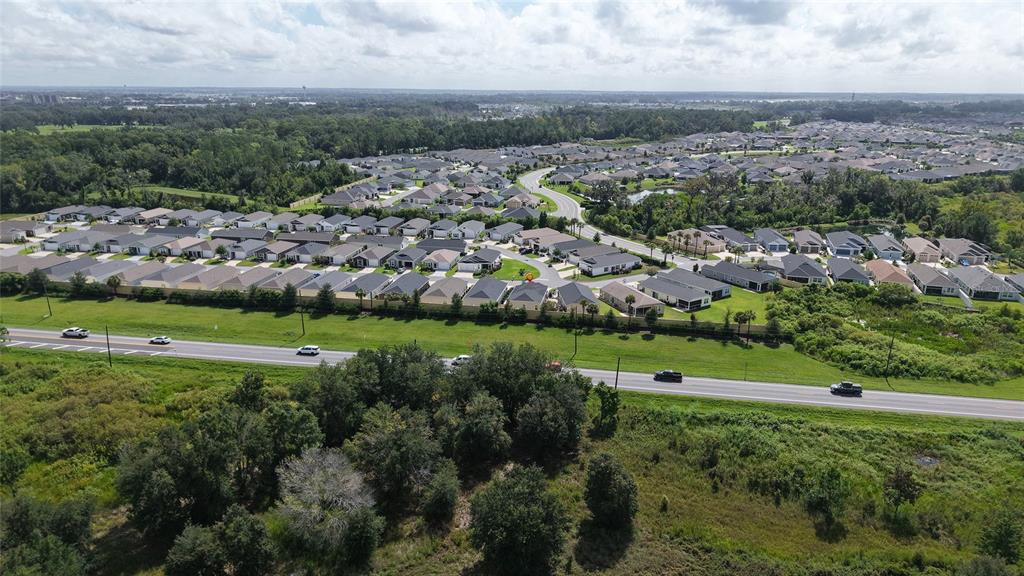 An aerial view shows a suburban neighborhood bordering a highway and wooded landscape — 4144 SILVANA WAY, THE VILLAGES, FL