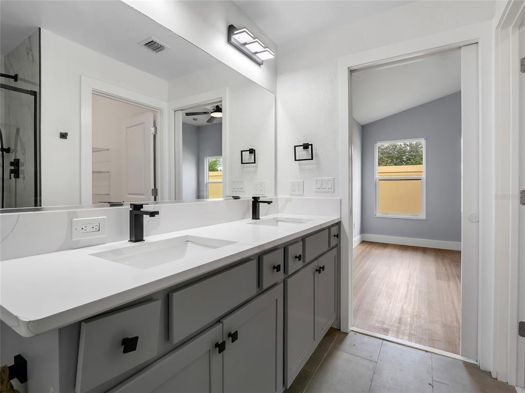 A bathroom features a double vanity with gray cabinets, white countertops, and black fixtures — 4144 SILVANA WAY, THE VILLAGES, FL