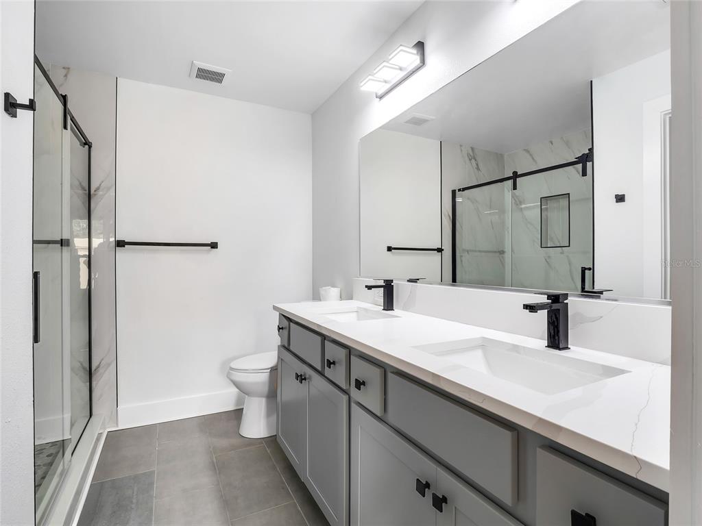 A modern bathroom features a double vanity with gray cabinets, white countertops, and a glass shower — 4144 SILVANA WAY, THE VILLAGES, FL