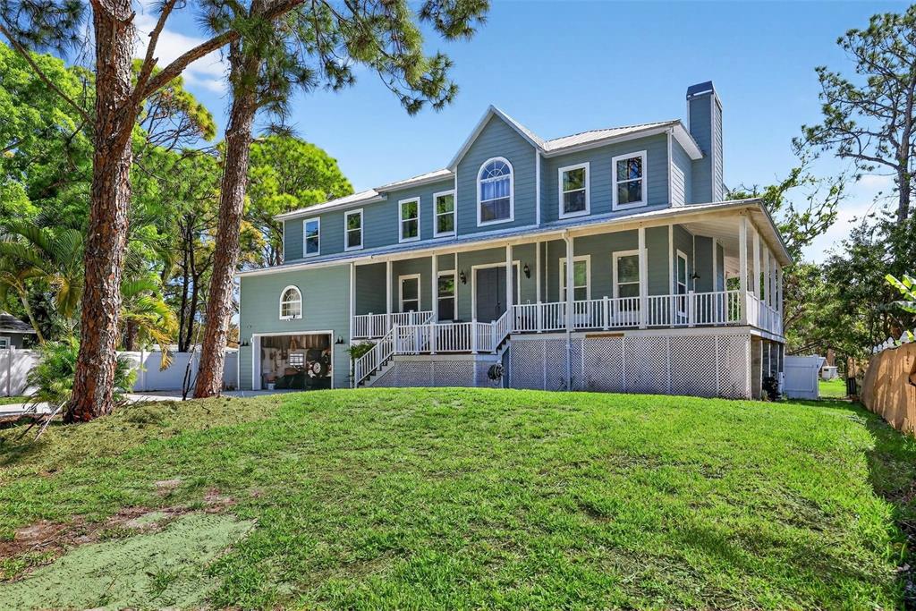A two-story blue house with a wrap-around porch and an attached garage sits on grass — 4433 SWEETWATER DRIVE, TAMPA, FL